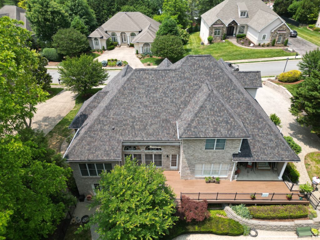 Drone view of a new gray roof on a large stone home with a back deck in Johnson City, TN